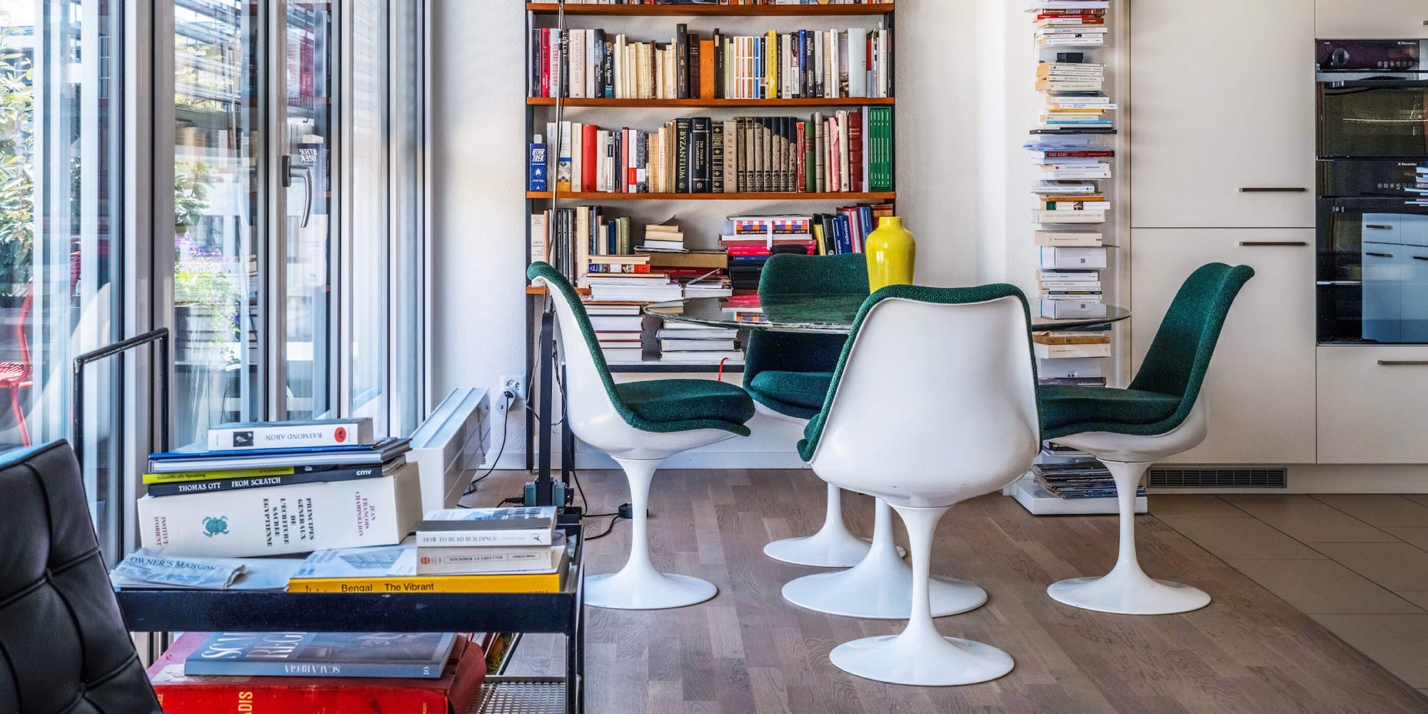 Grüner, runder Steintisch mit 4 Stühlen aus den 60er Jahren stehen vor einem vollem Bücherregal am Fenster. 