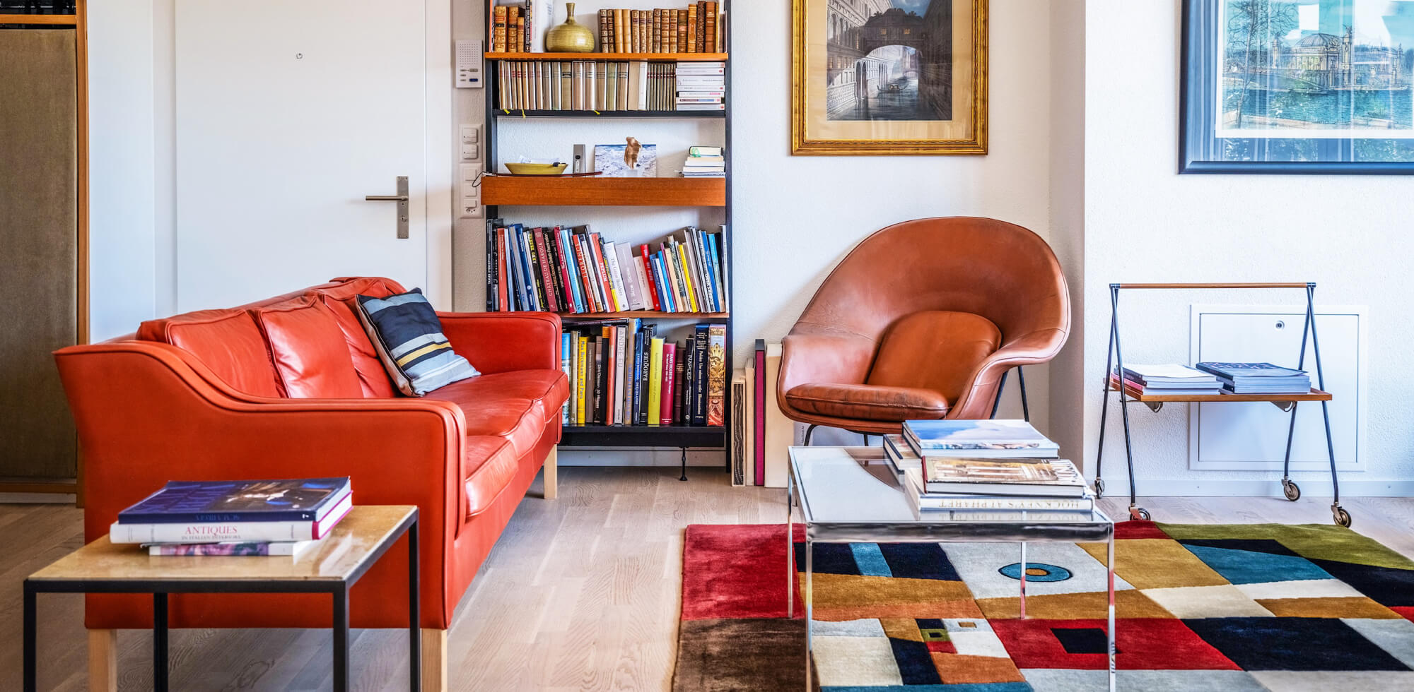 Wohnung als Bühne für Designgeschichte. Designermöbel aus verschiedenen Epochen, rotes skandinavisches Sofa, brauner Ledersessel und bunter Teppich. 